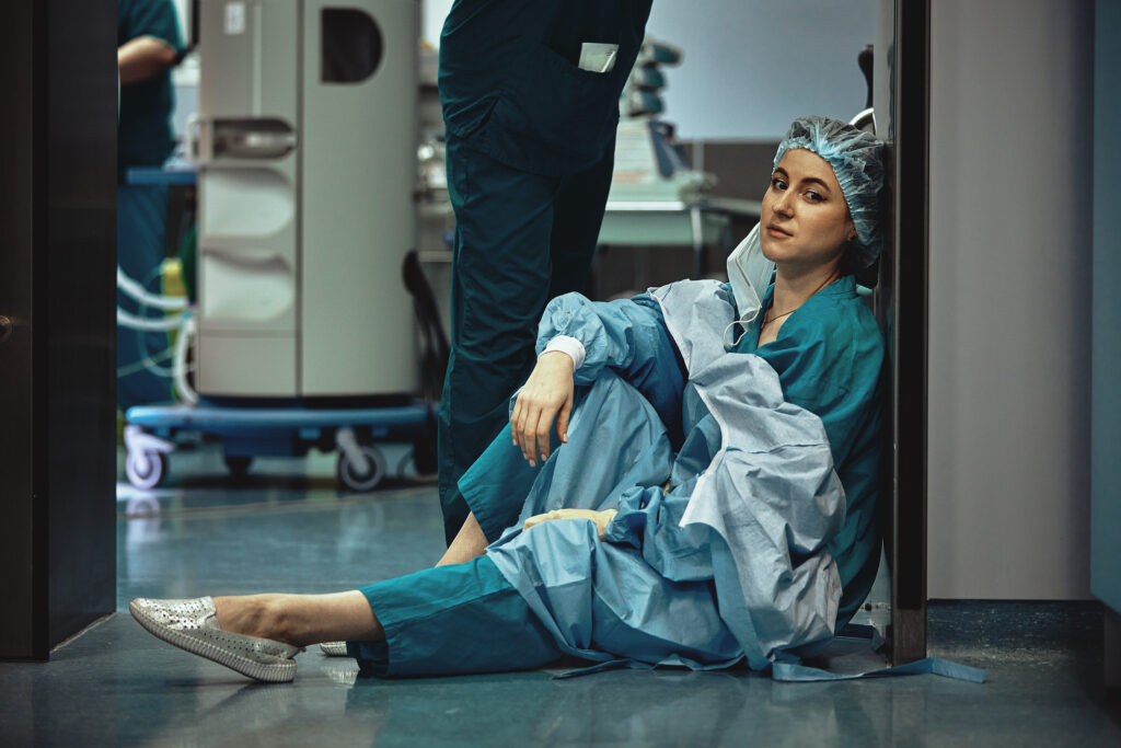 Tired doctor sitting after surgery in the hospital corridor. Great burden on doctors and medicine. Rest after work. Epidemic, lack of medical personnel, medical wards